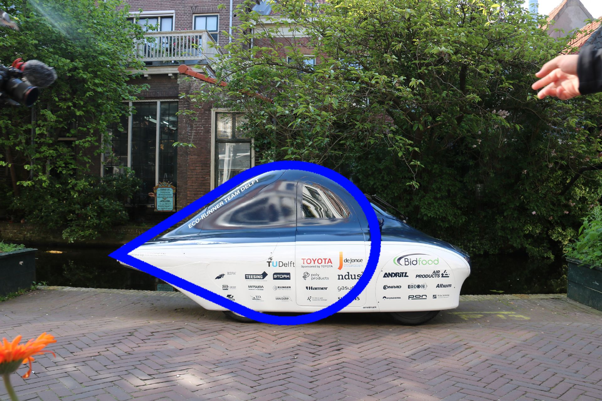 Ecurunner Team Delft, geparkeerd in Nederlandse straat. Druppelvorm eroverheen getekend, de contouren van het voertuig volgend.